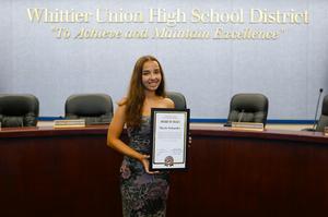 Whittier Union High School District student Marle Schaefer smiles while holding an Award of Merit certificate in the District’s Board of Trustees meeting room.
