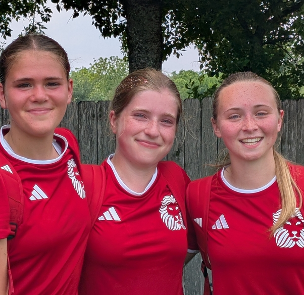 Three girls smile at camera, wearing red soccer jerseys