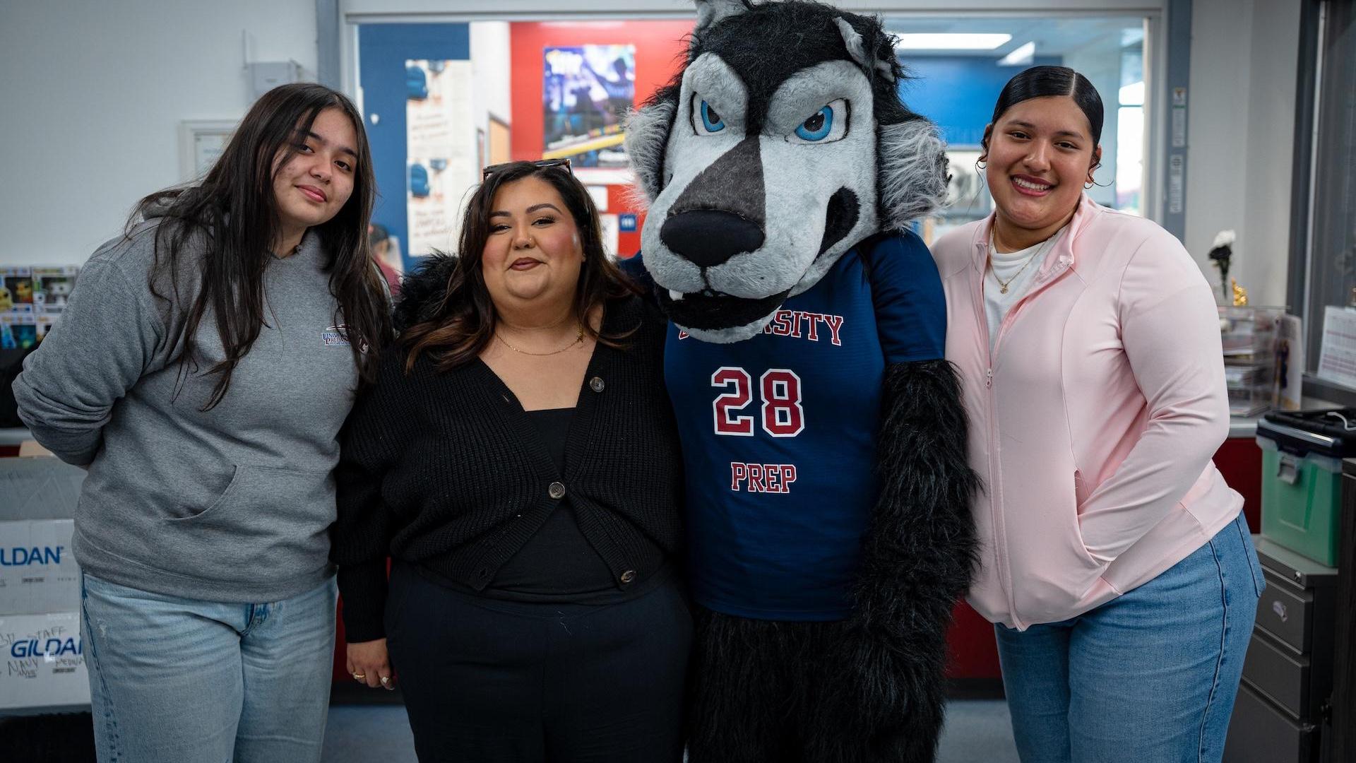 Three people pose with a wolf mascot in a school setting.
