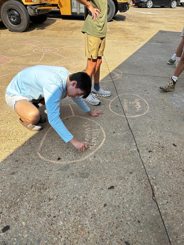 Student writing on concrete outside with peach-colored  chalk