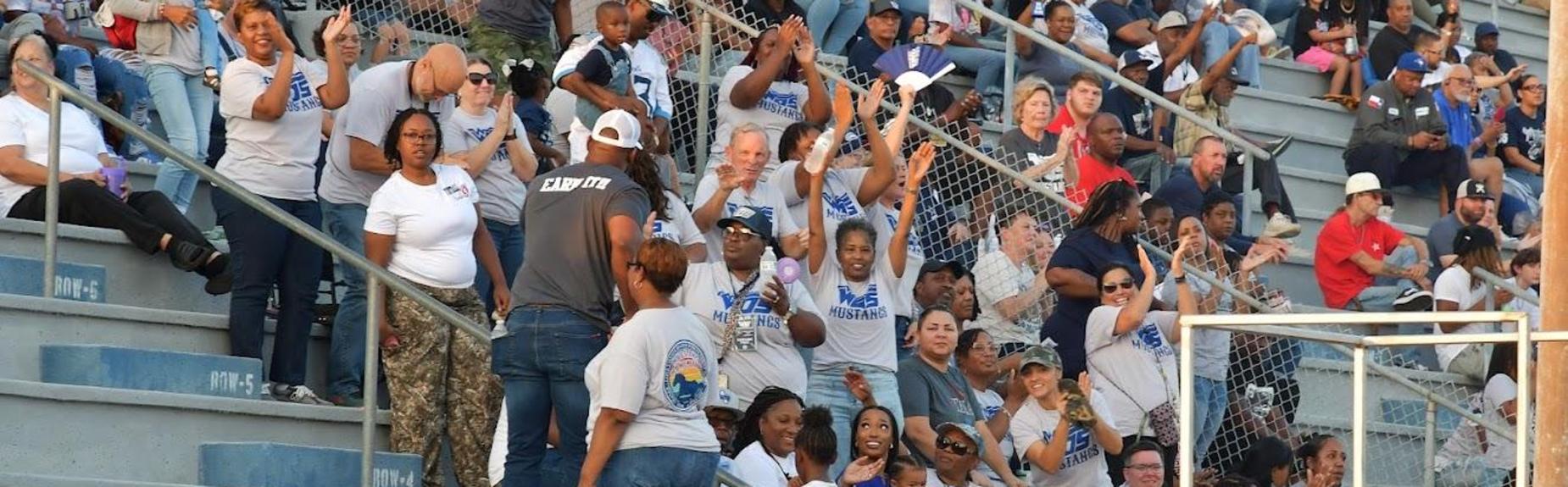 Cheering crowd wearing matching shirts at a sports event.