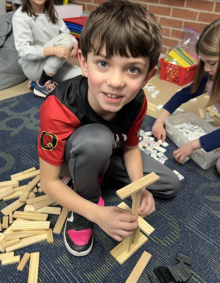 Young boy smiles while building with wooden blocks on a classroom floor.