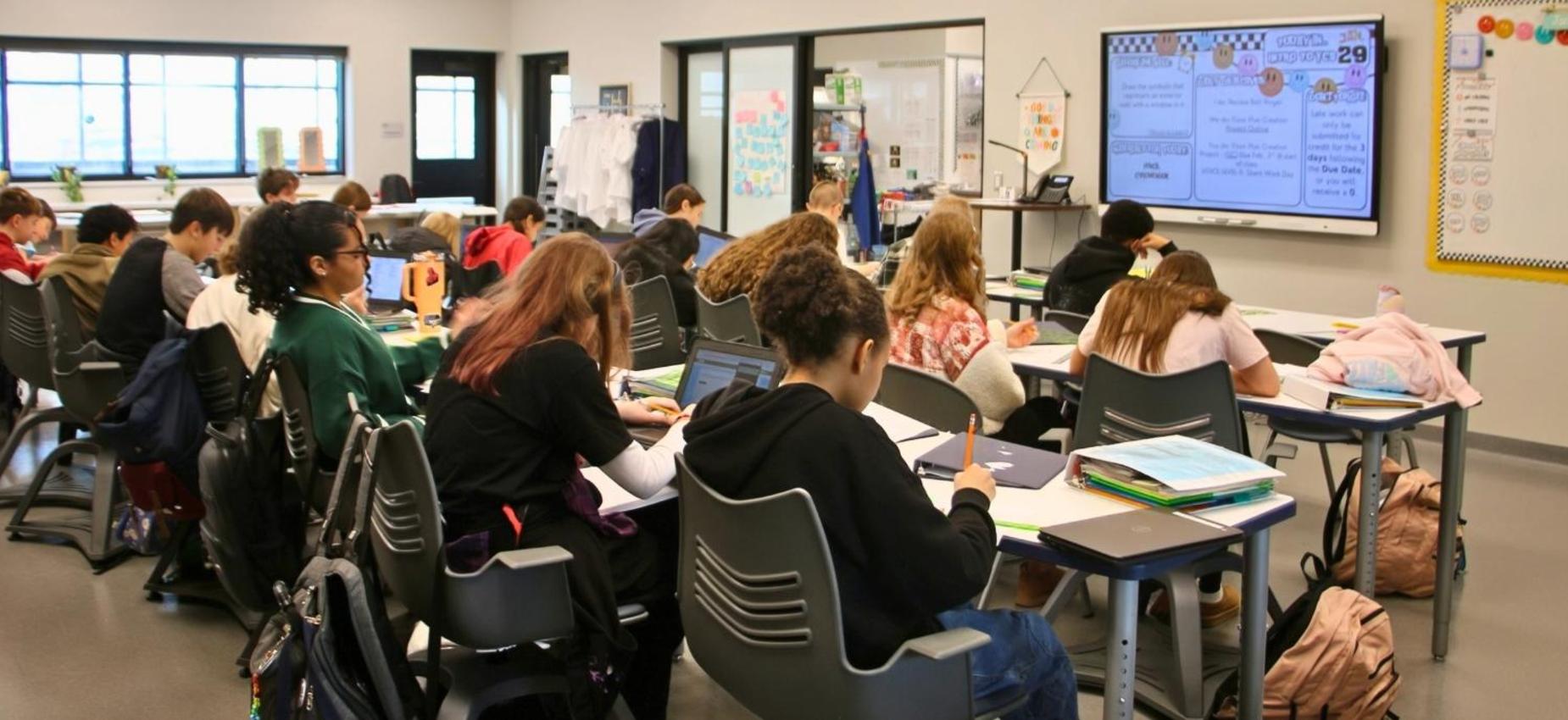 Students engaged in writing at desks in a classroom.