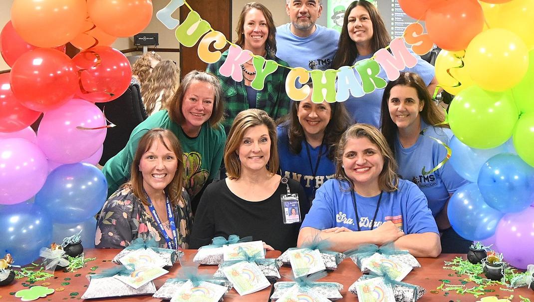 Group of people posing with colorful decorations and party favors at an event.