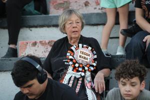 An elderly woman sits in the stands wearing a decorative ribbon.