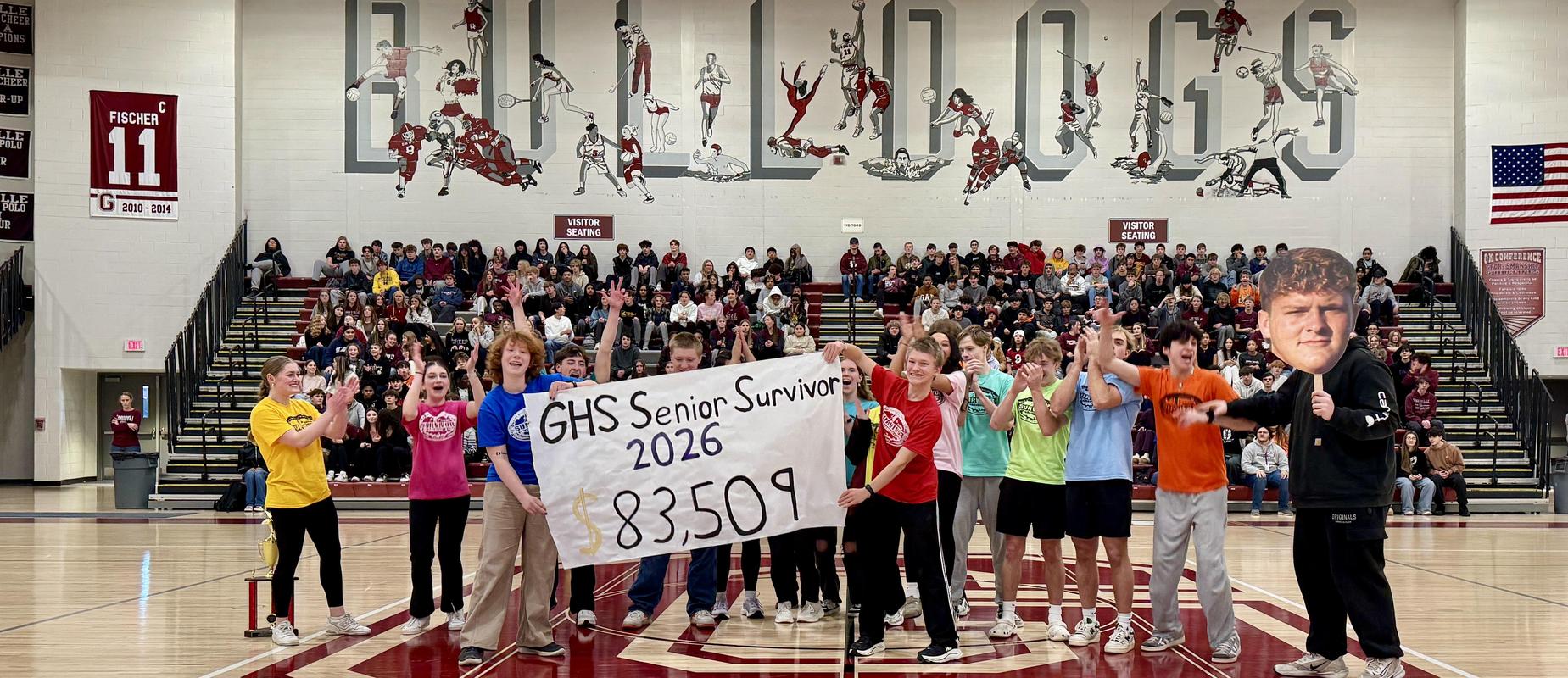 Grandville Senior Survivors hold up sign that says $83,509 and 16 seniors are clapping in the middle of the gym
