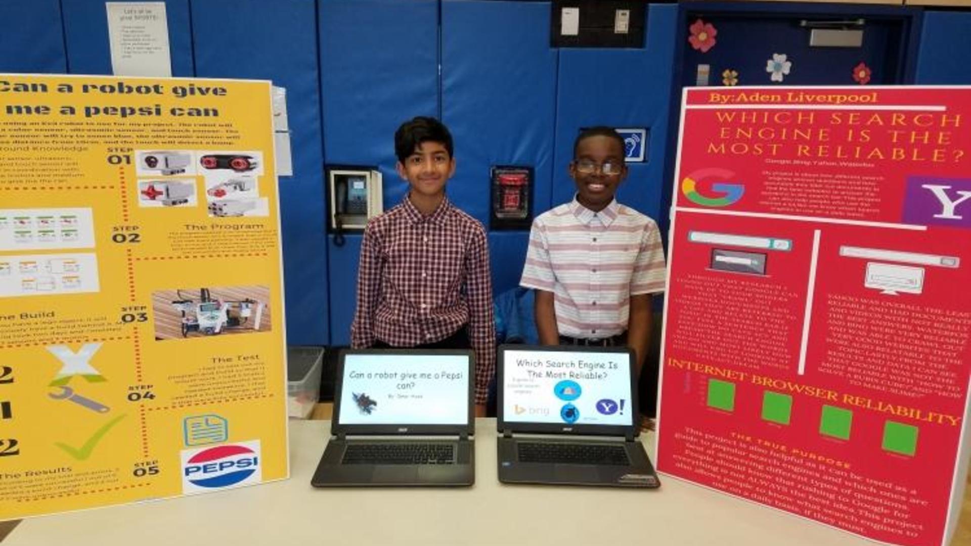 Two students presenting projects next to colorful display boards.