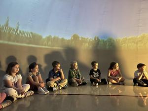 Children sitting on the floor in a softly lit room, engaged and watching.