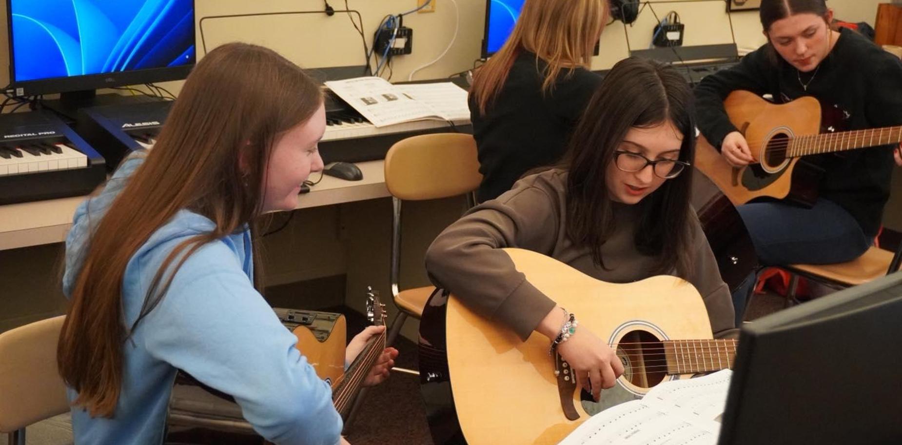 girls play guitars with music in front of them