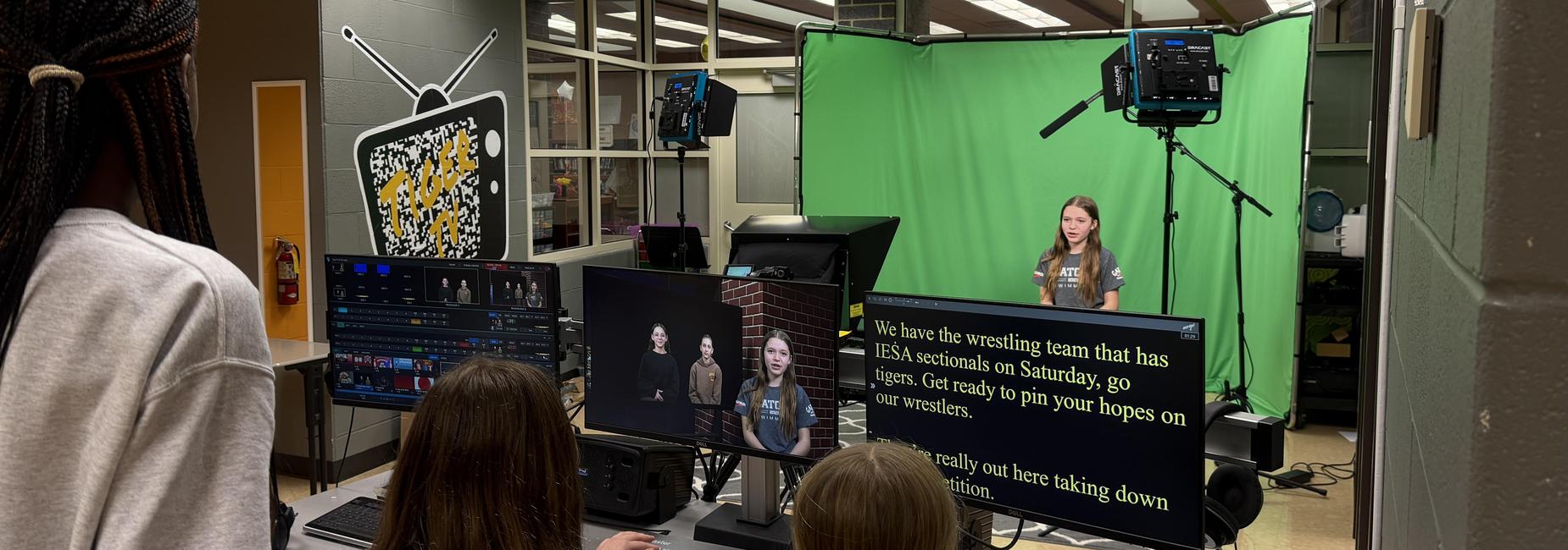 A girl stands in front of a green screen with cameras and monitors in a studio.
