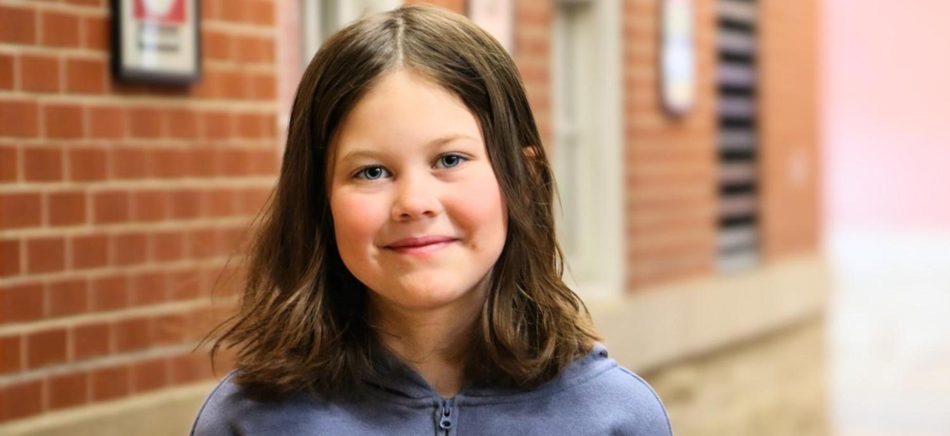 A young girl smiles while standing in a school hallway.