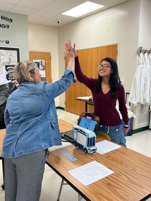 Two women exchanging high fives in a classroom during an interactive activity.