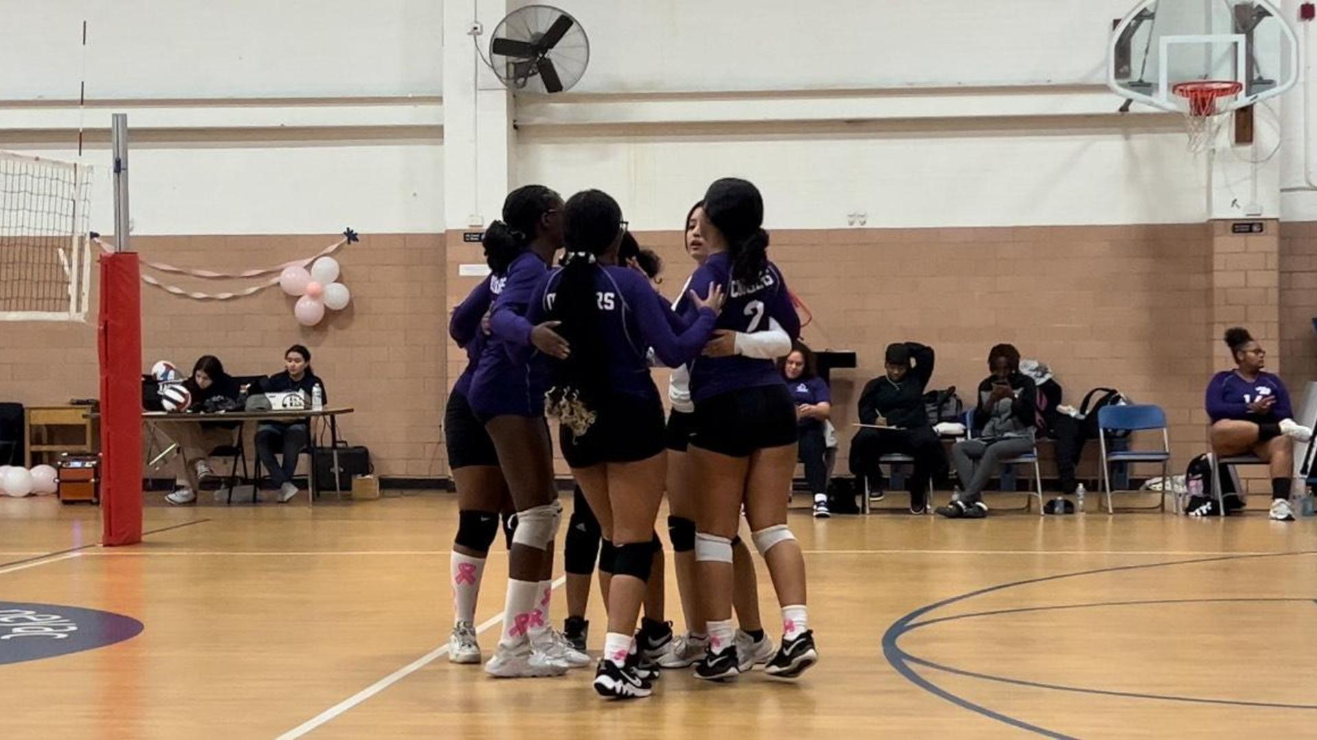 A group of volleyball players huddled together on the court in team uniforms.