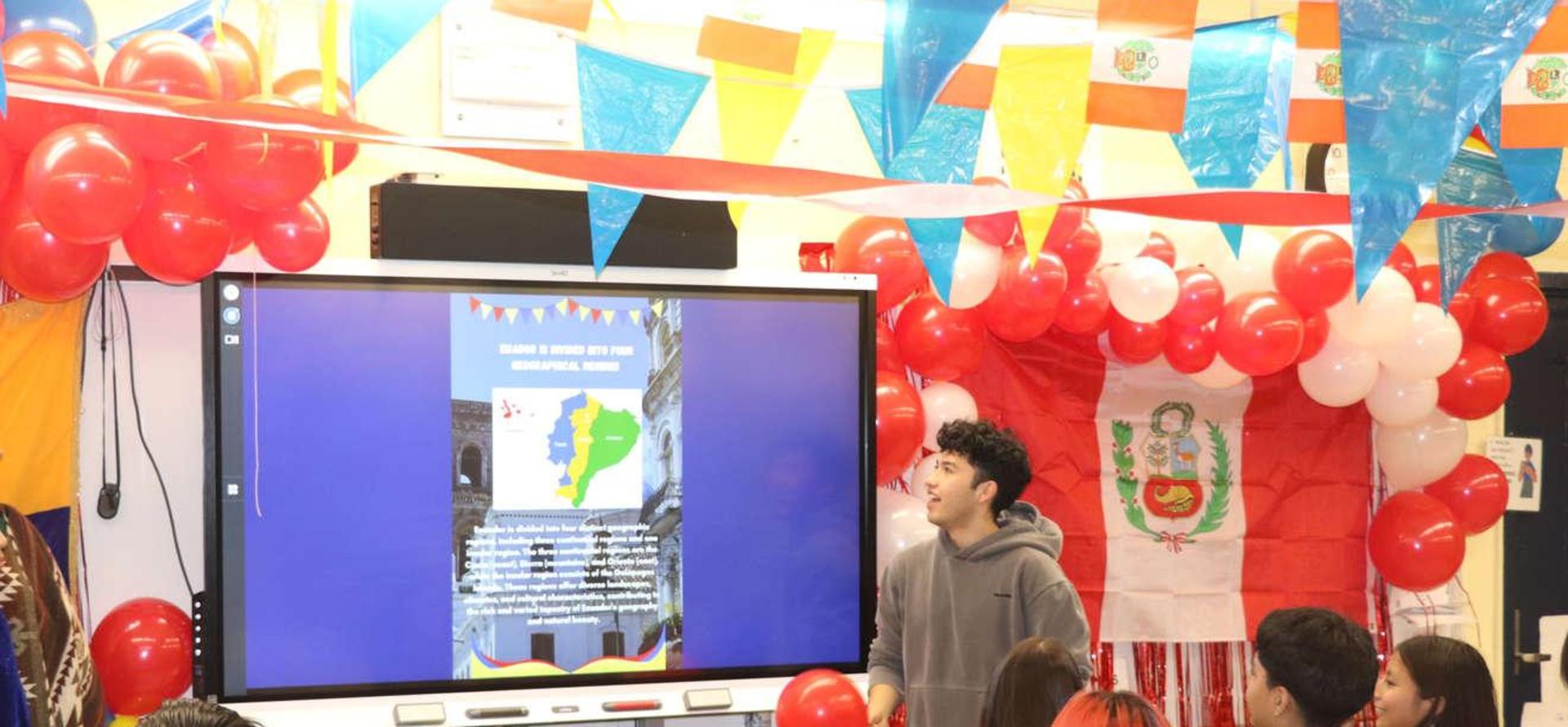 A presenter speaking in front of a screen with cultural decorations.