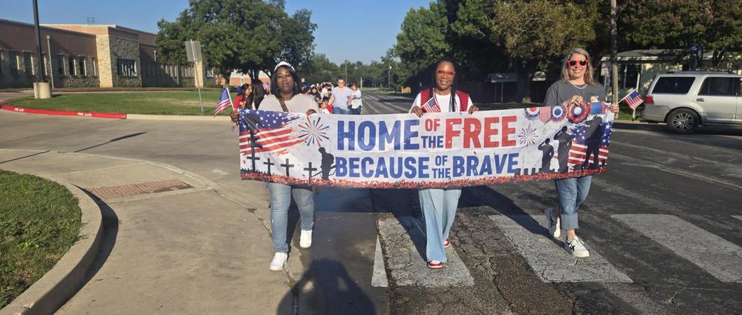 Admin staff holding a Home of the Free because of the Brave banner.