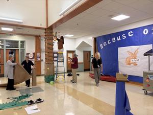 Multiple people decorating a space with paper leaves and a large banner.