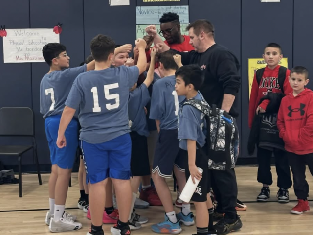 Youth team huddles together with coaches in a gym.