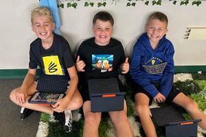 three students sit on the floor holding their iPads