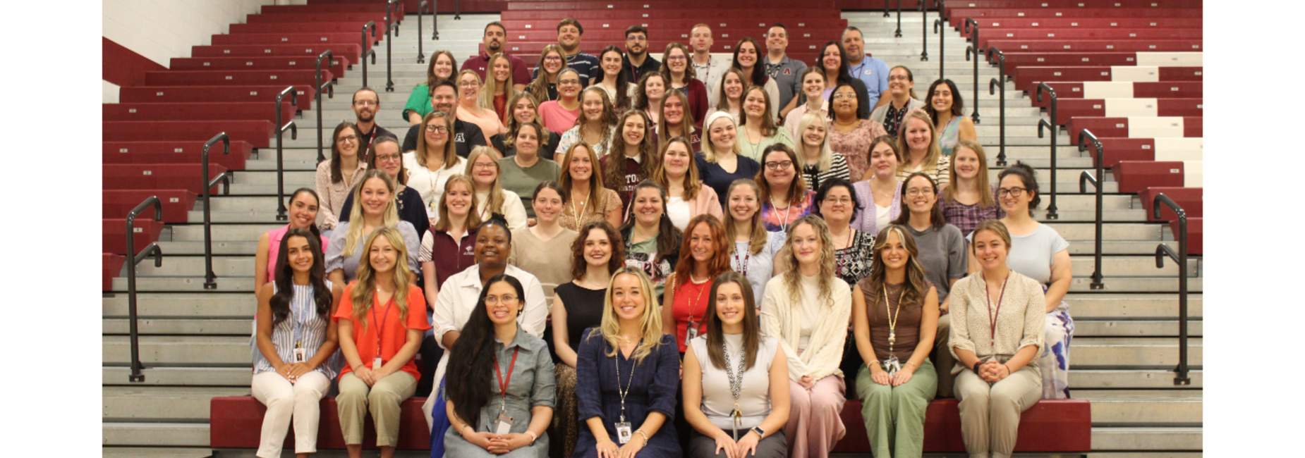 Large group of diverse people posing together on gym bleachers. - 2026 New Teacher Induction