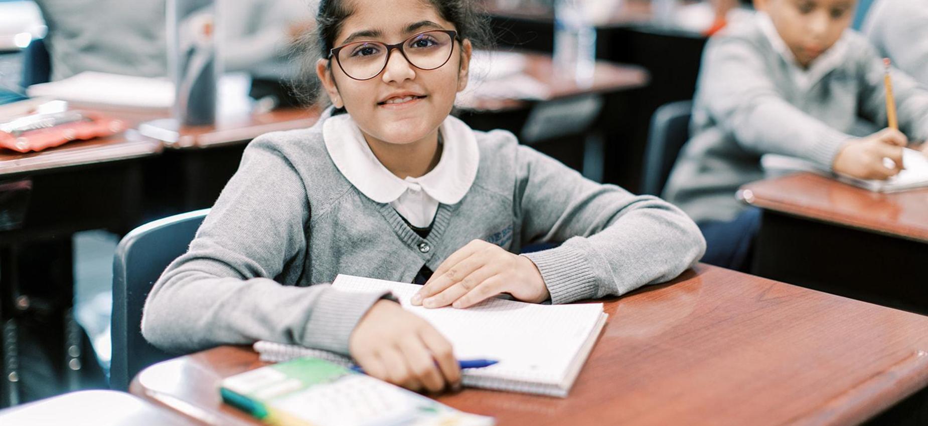 Smiling student with glasses writes at her desk