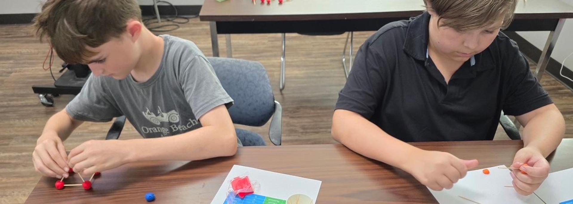 Two boys building with colorful modeling materials and toothpicks at a table.