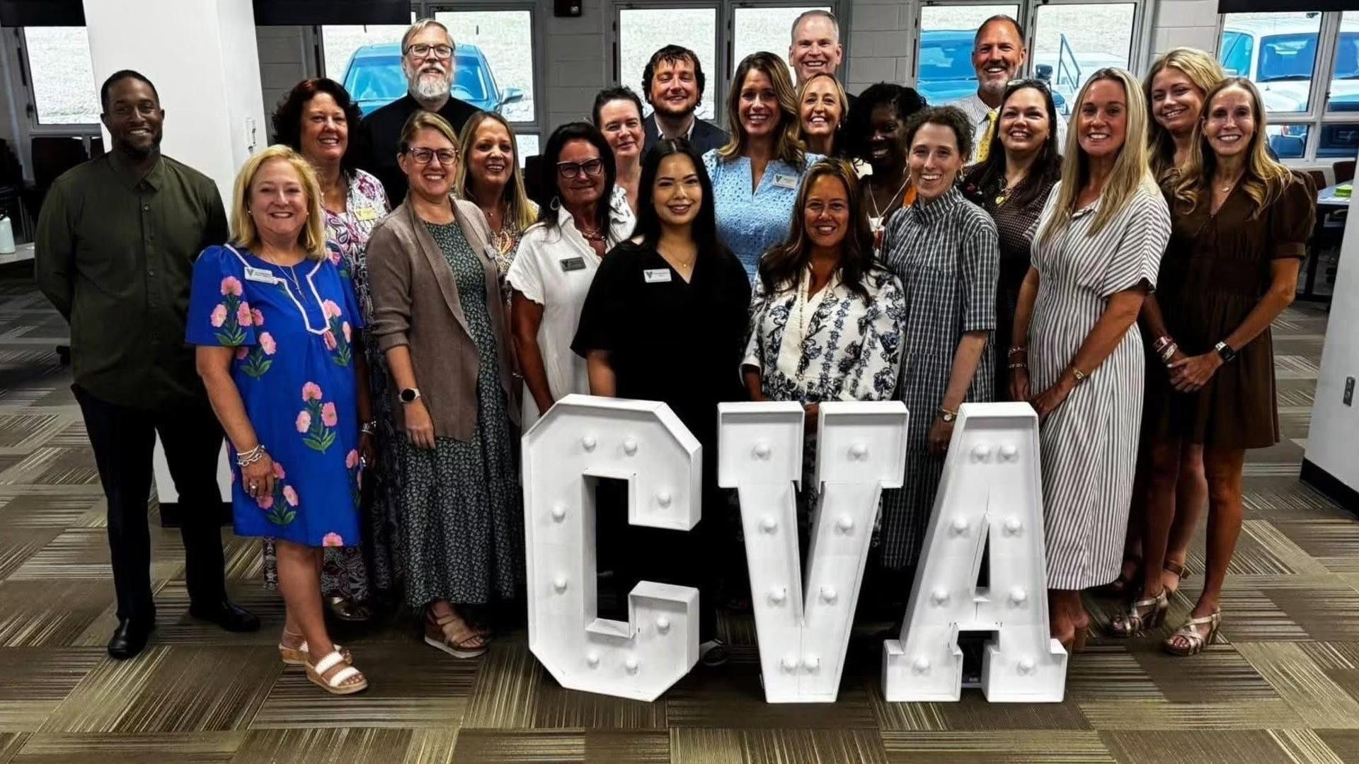 A group of smiling individuals posing together around large lighted letters spelling 'CVA'.