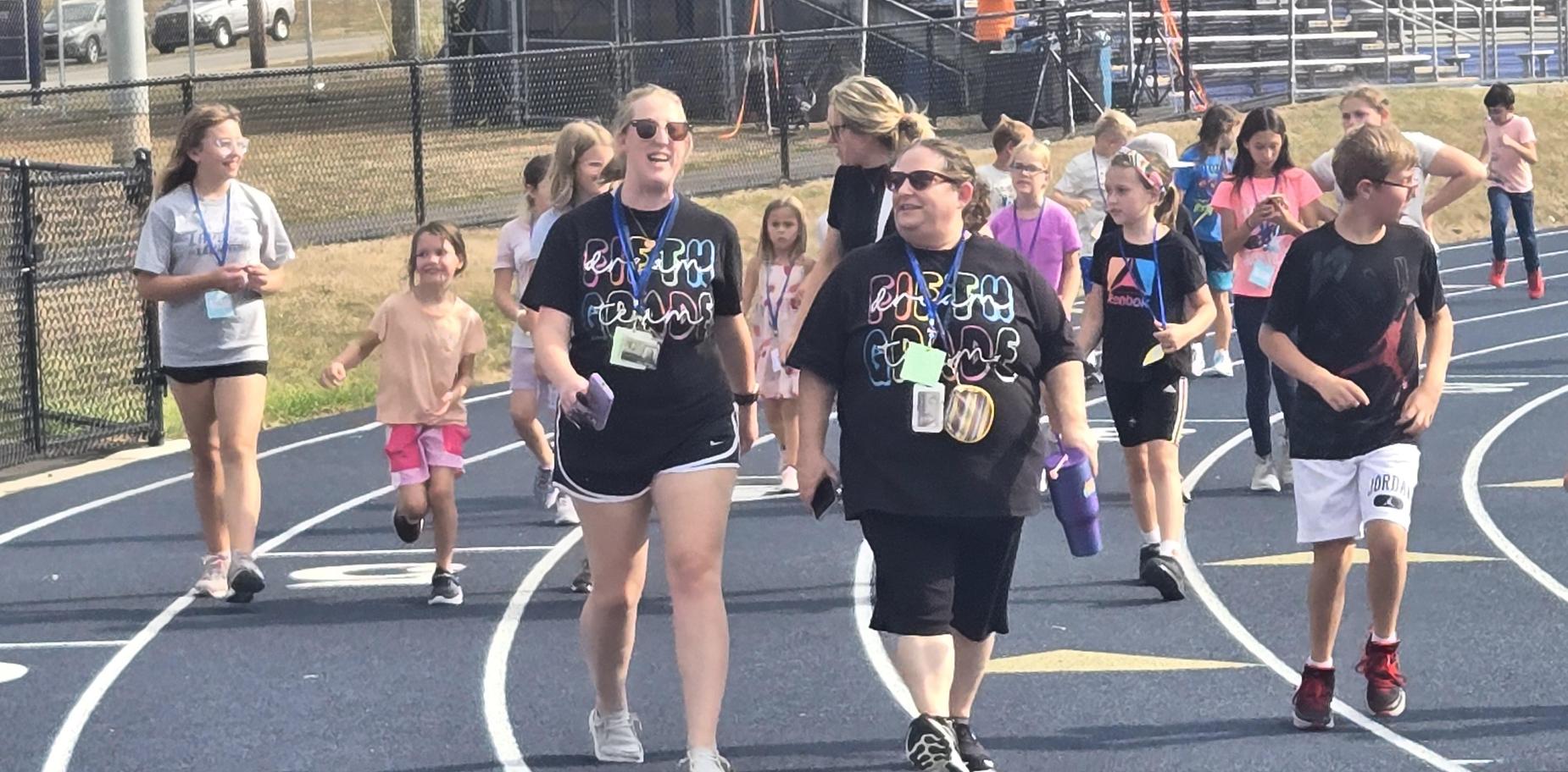 Teachers and students walking on a track at a school event, smiling and enjoying the day.