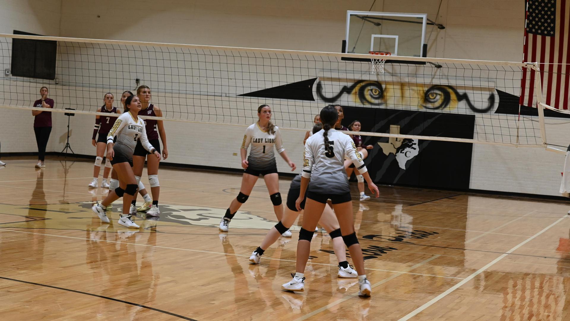 Female volleyball players in action during a game in a gymnasium.