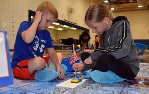Boy and girl build a model with blocks and a flag on a lunar-themed surface.