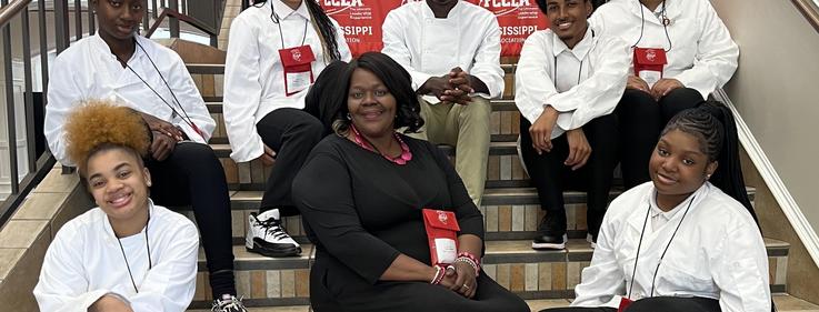 Group of people sitting on stairs, smiling, in a well-lit indoor space.