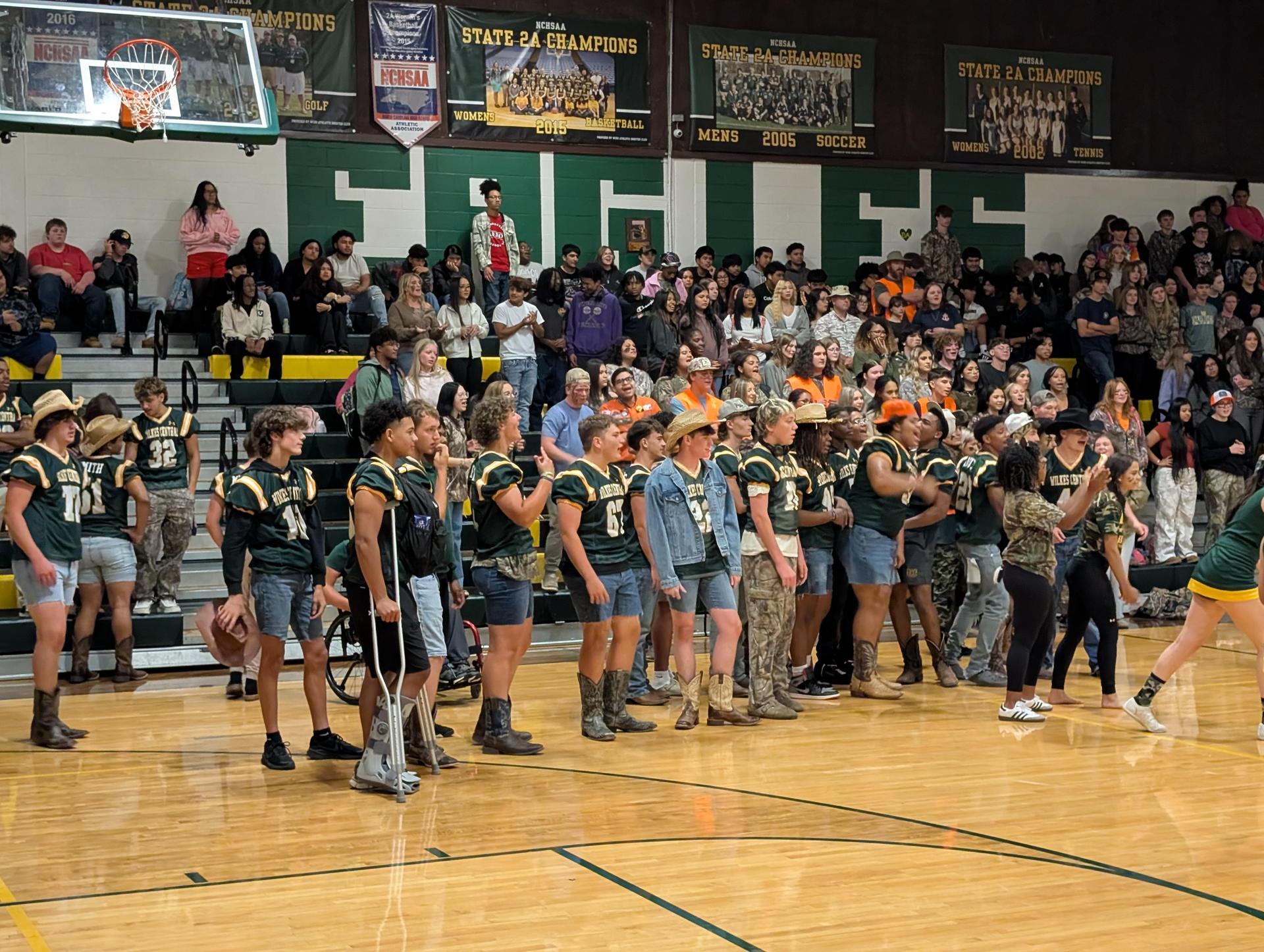 Cheering crowd and students in school spirit attire at a gymnasium event.