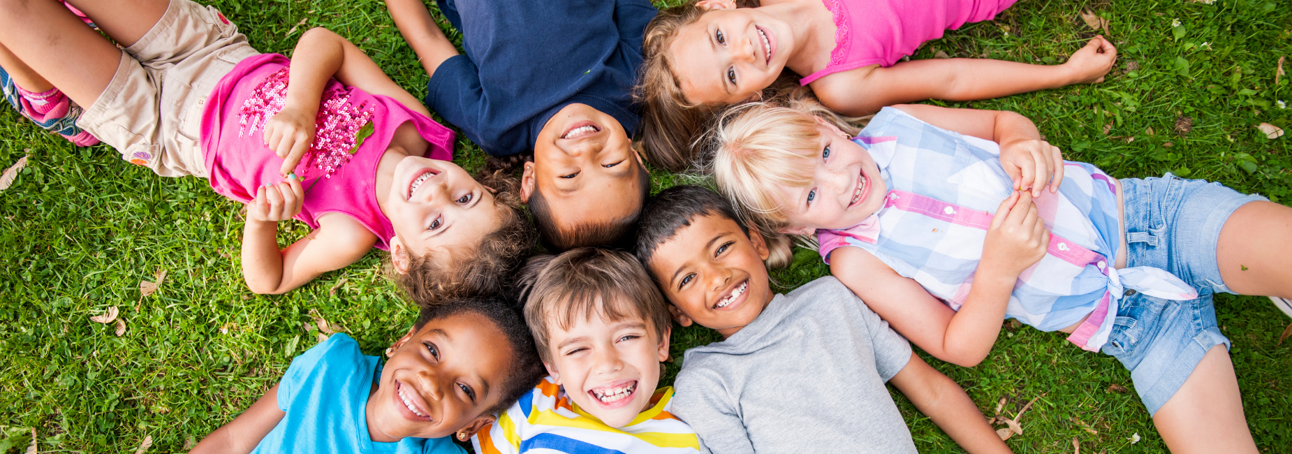 7 young kids lying in the grass with their heads together