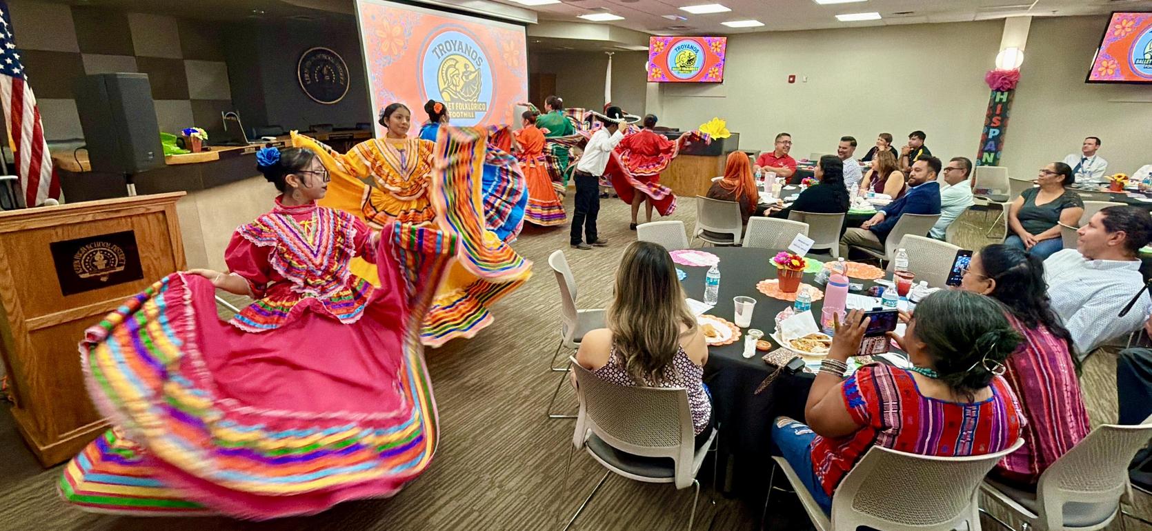 Cultural event with dancers in colorful dresses performing in front of an audience.
