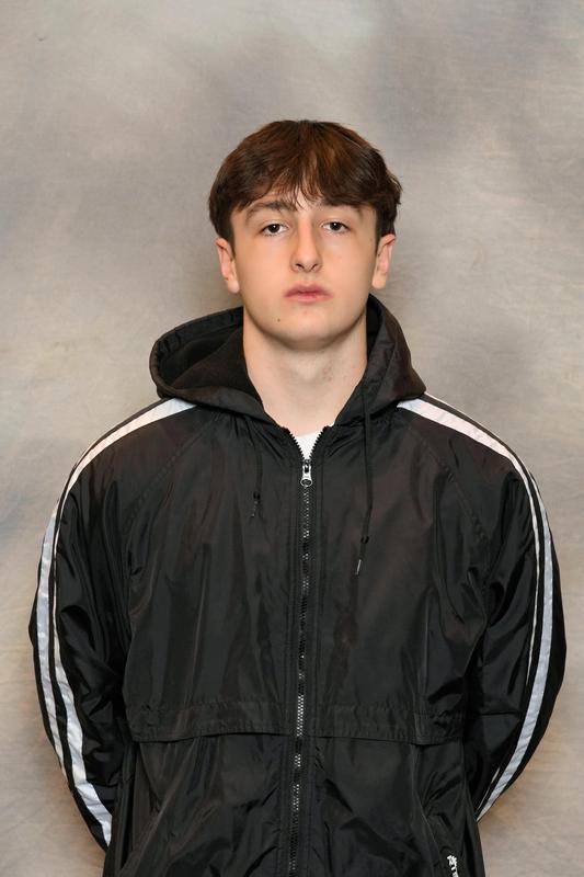 Male athlete stands with arms behind his back in black jacket