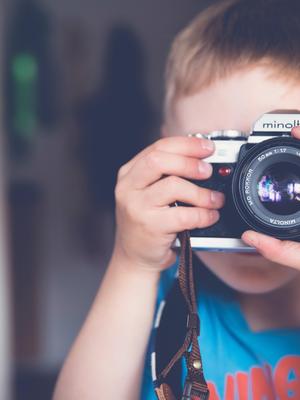 Child holding a camera and looking through the viewfinder.