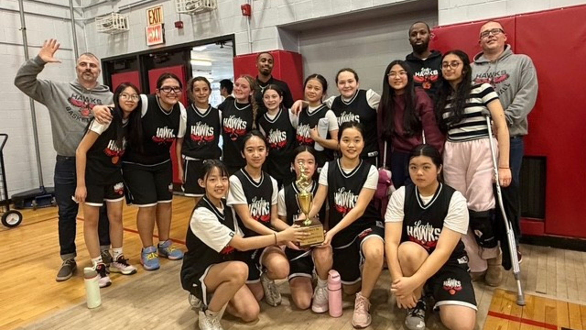 A group of basketball players and coaches celebrating with a trophy.