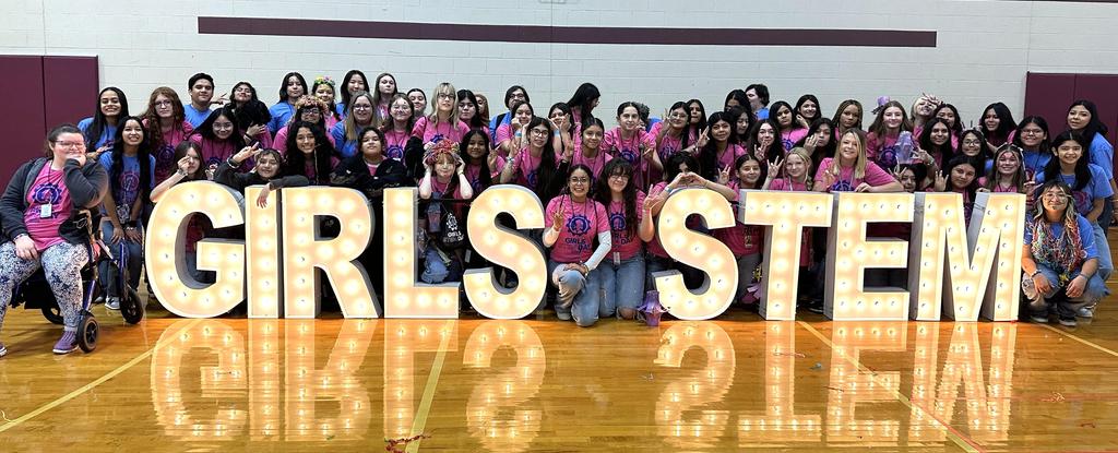 Group of diverse girls posing with illuminated letters spelling 'GIRLS STEM'.