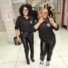 Two women in matching outfits posing playfully in a school hallway.