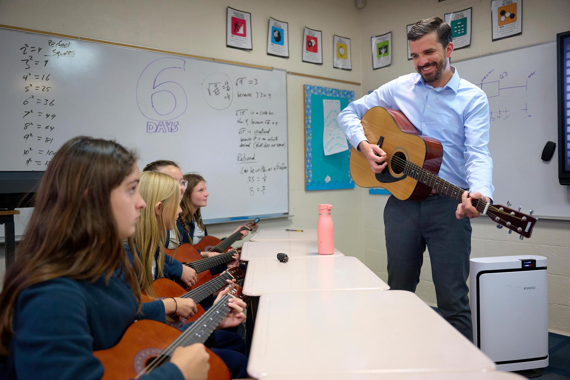 middle school girls in guitar music elective with teacher demonstrating