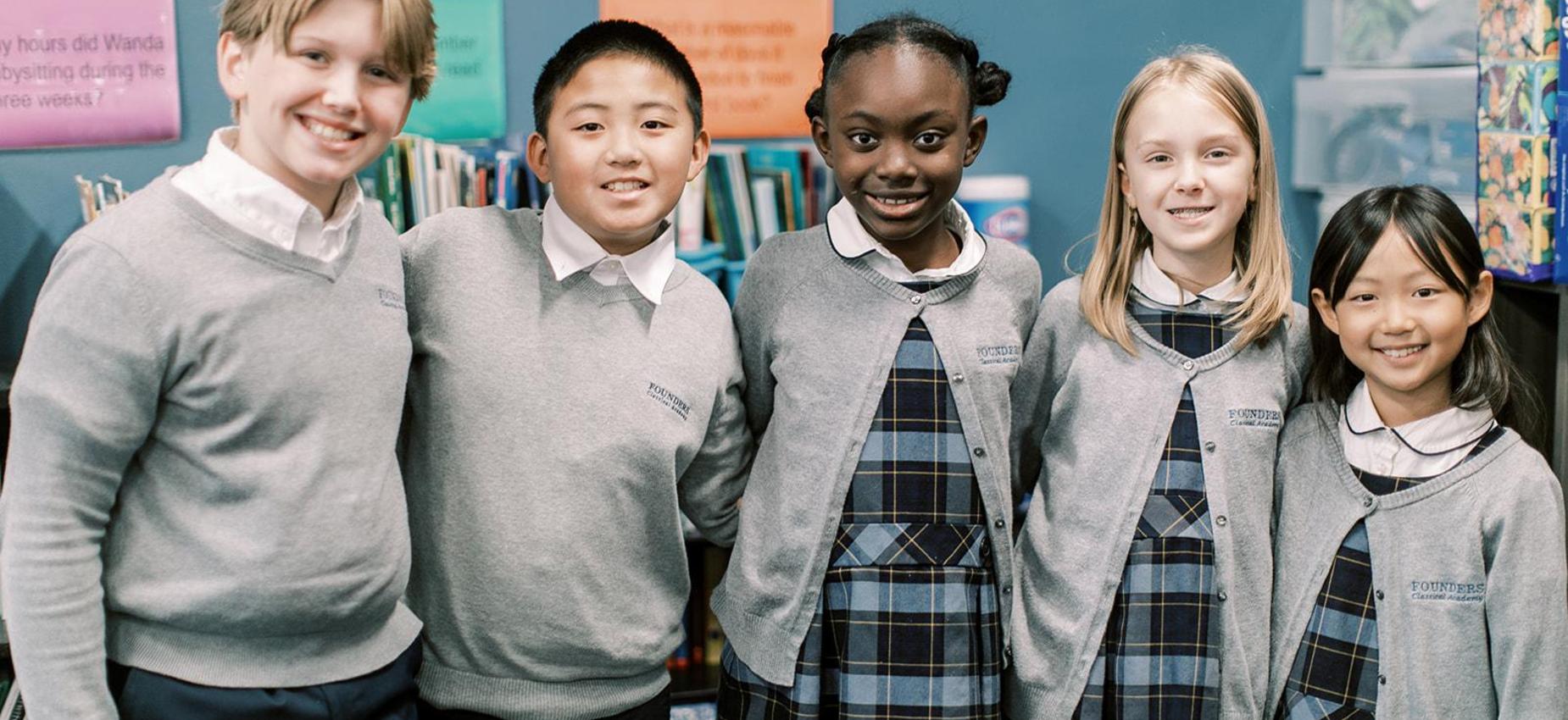 Five smiling elementary students stand together in front of a bookshelf