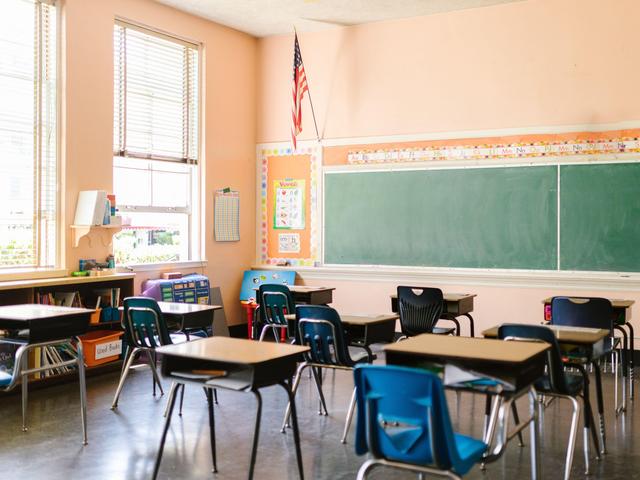 Empty classroom with desks, chalkboard, and an American flag.