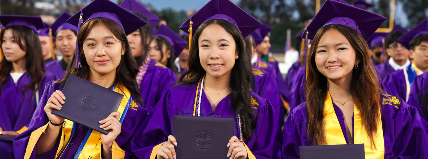 Graduates in purple caps and gowns holding diplomas, smiling at the camera.
