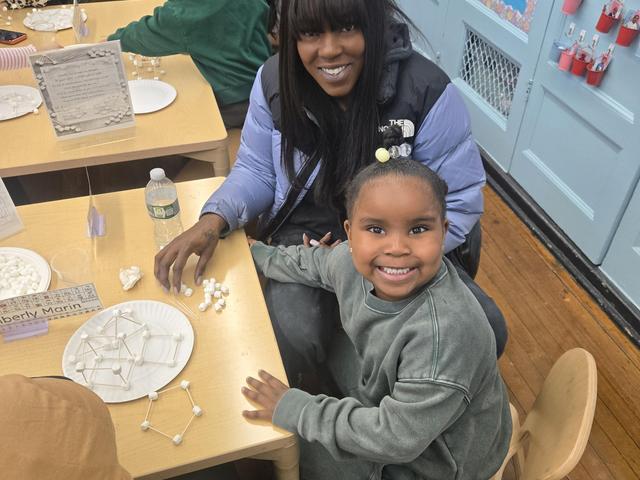 A woman and a girl smiling while working on a craft project at a table.