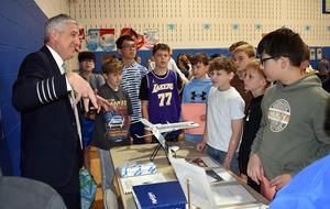 A group of students listening intently to a pilot explaining an aircraft model.