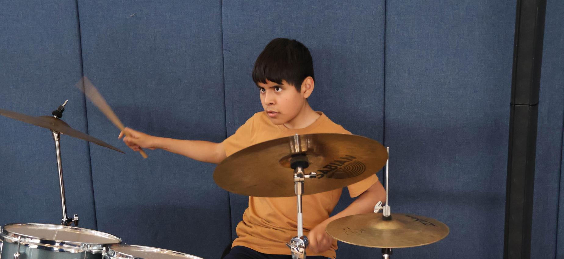 Boy playing drums energetically at a music session.