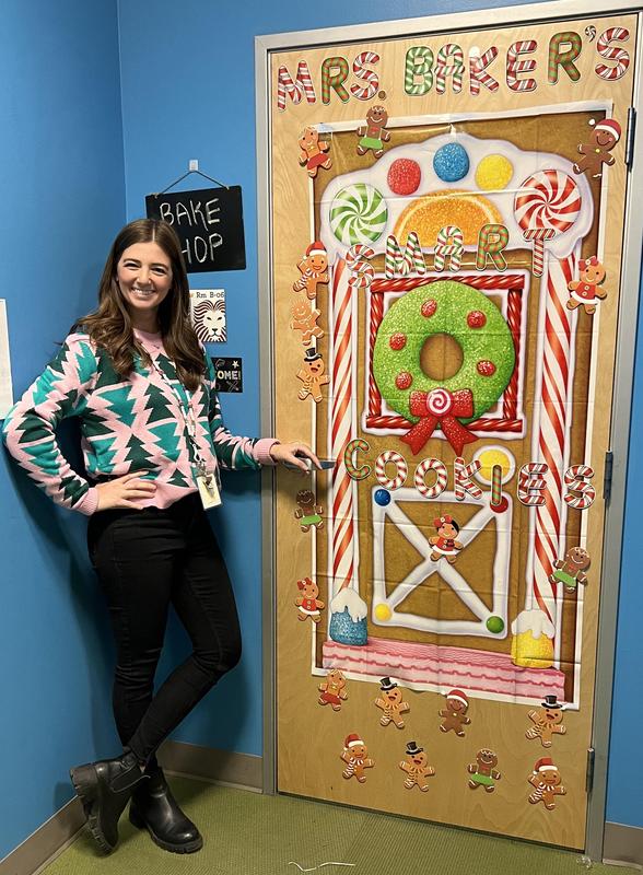 Ms. Baker stands next to her door, covered like a gingerbread house