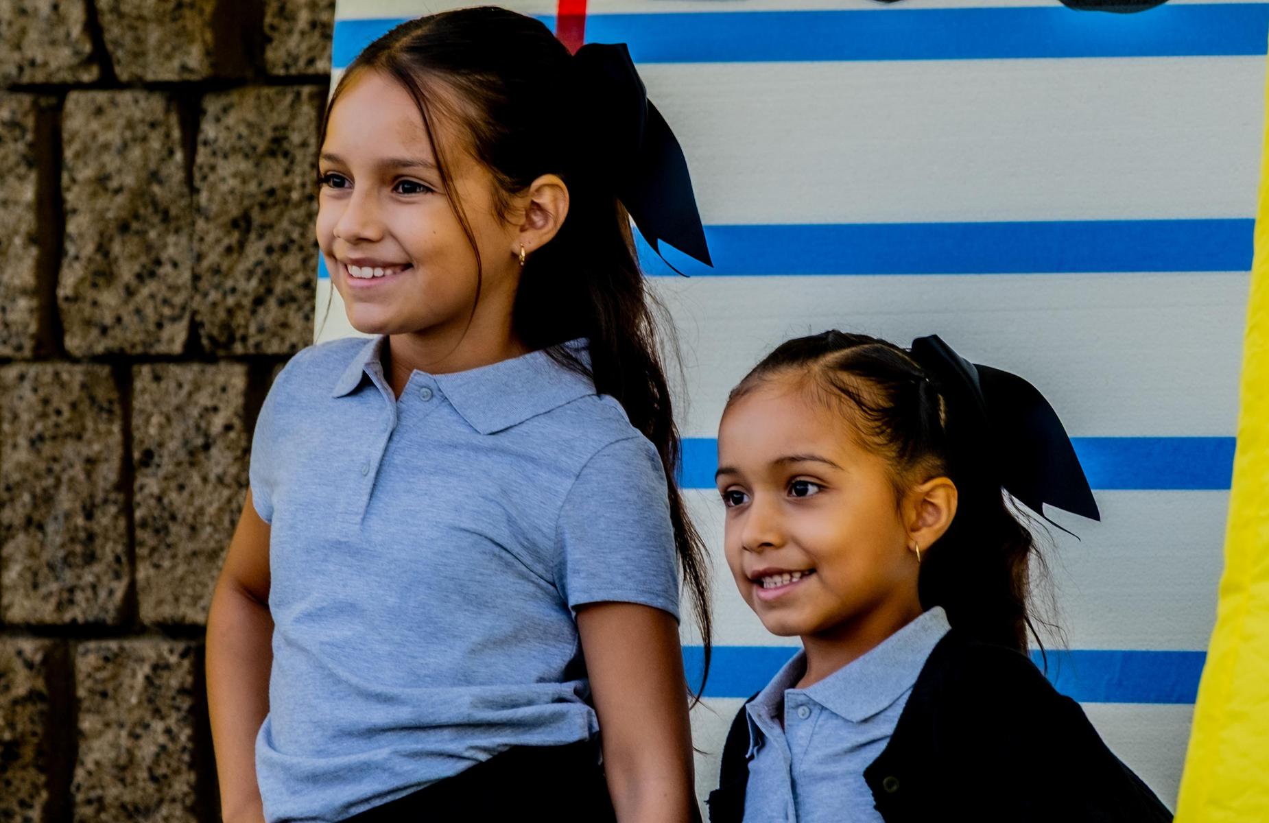 Two female students smile and take photos against backdrop