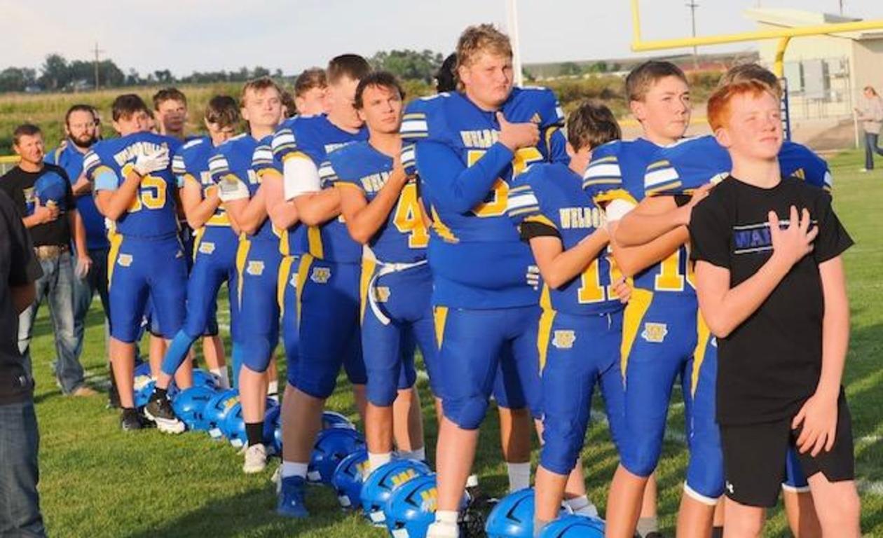 A group of young football players standing in line with helmets on the ground, during the national anthem.