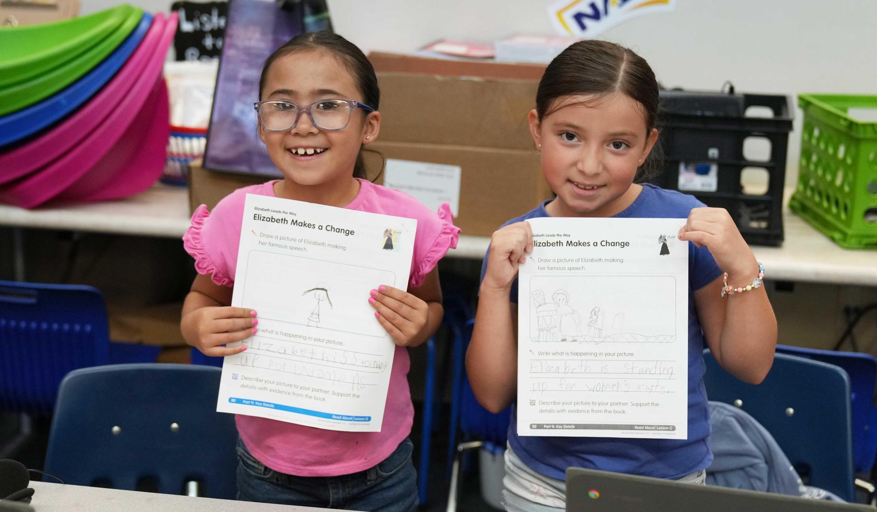two girls holding up completed assignment