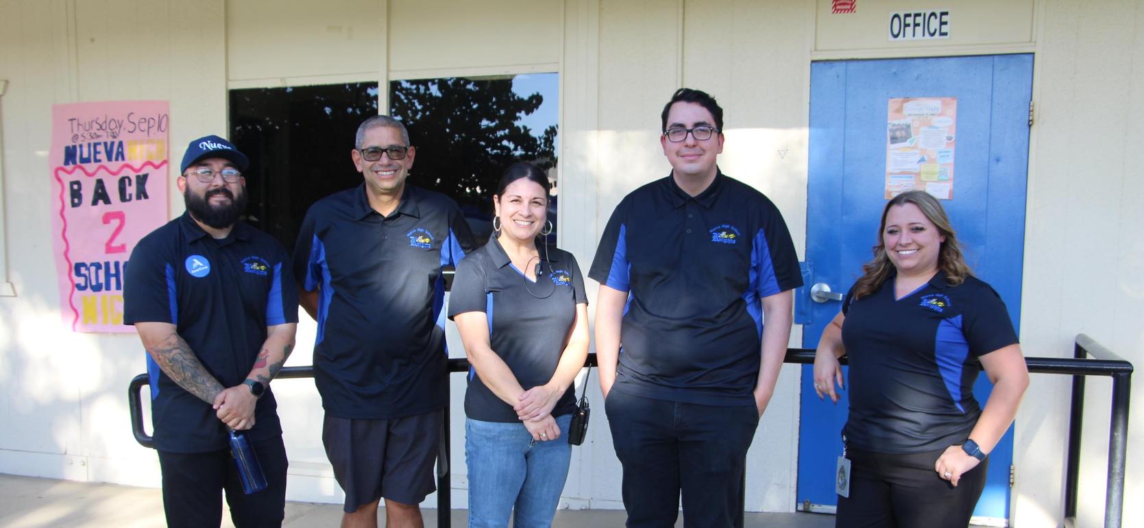 Group of five people standing outside a school with blue doors.